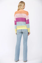 Back view of a woman wearing an open weave color block striped sweater and jeans on a white background
