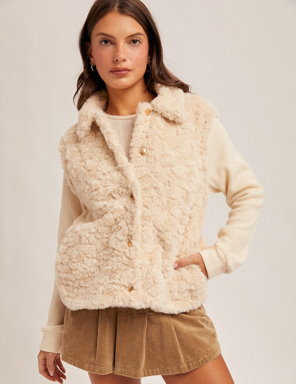 Woman wearing an ecru faux fur and knit sleeves jacket and  brown skirt on a white background