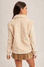 Back view of a woman wearing an ecru faux fur and knit sleeves jacket and  brown skirt on a white background