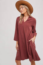 Woman wearing a wine colored dress and brown hat on a white background