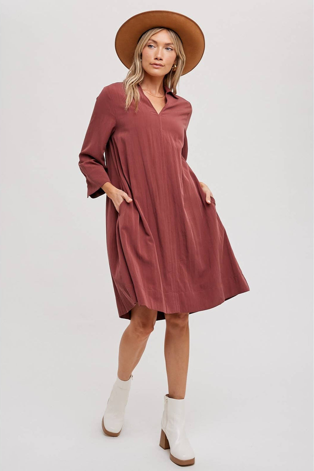 Woman wearing a wine-colored dress, white boots, and a brown hat on a white background