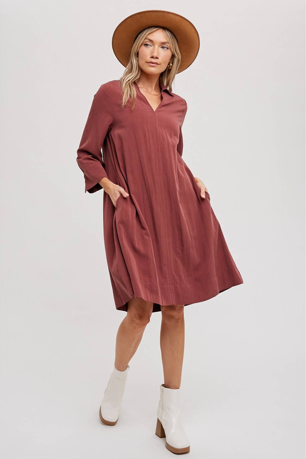 Woman wearing a wine-colored dress, white boots, and a brown hat on a white background