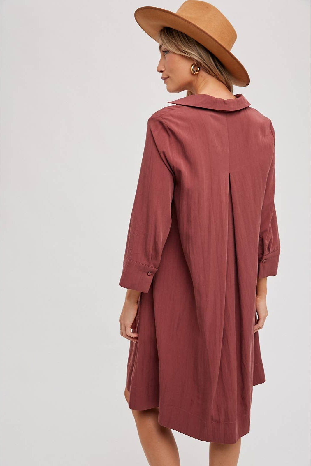 Woman wearing a wine-colored dress and brown hat on a white background