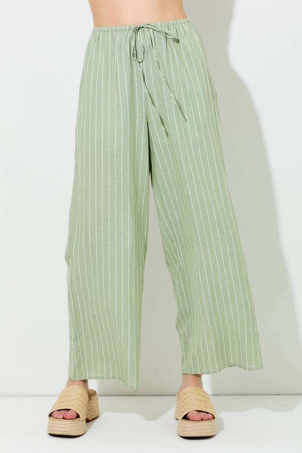 Woman wearing pin stripe green and ivory wide leg pants on grey background