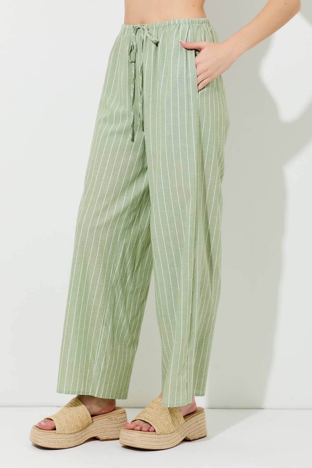 Woman wearing pin stripe green and ivory wide leg pants on grey background