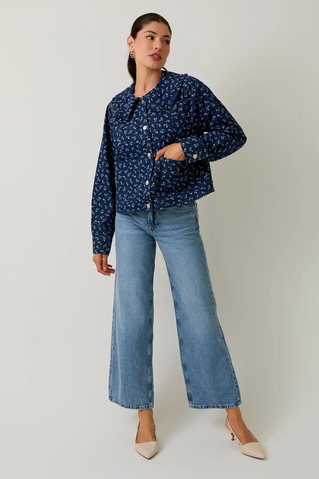 Woman wearing a medium denim blue floral jacket and blue jeans on a white background