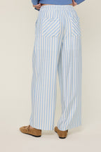 Back view of a woman wearing sky blue and cream striped wide-leg pants on a plain background