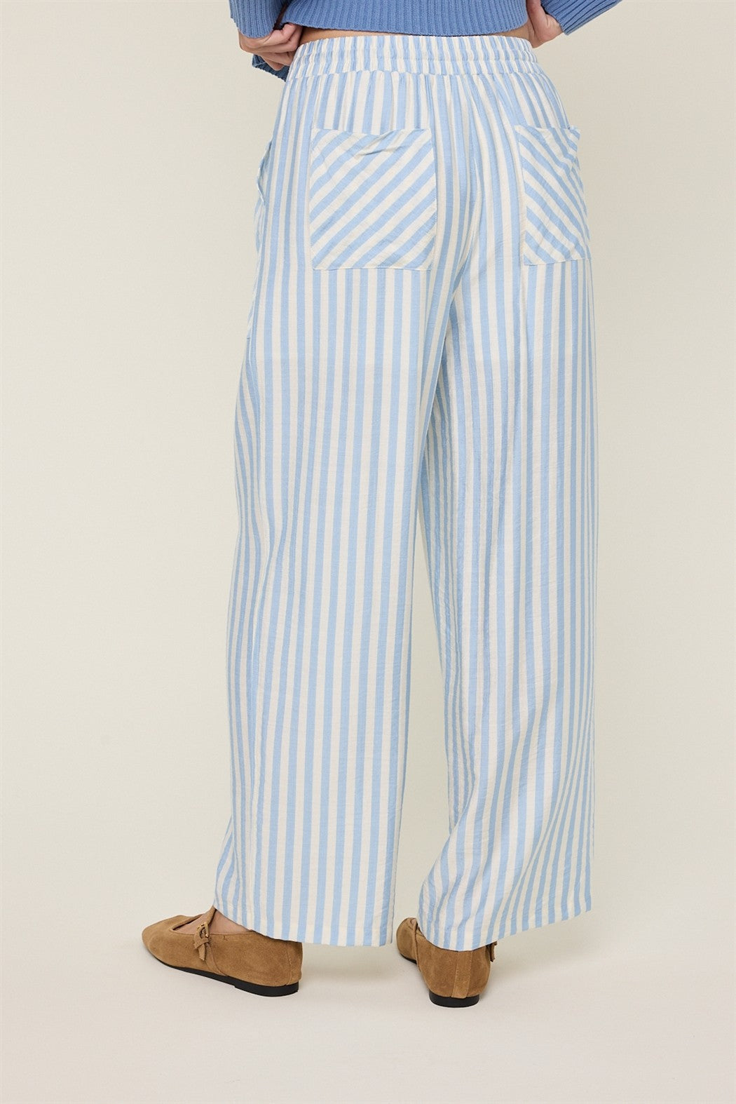 Back view of a woman wearing sky blue and cream striped wide-leg pants on a plain background