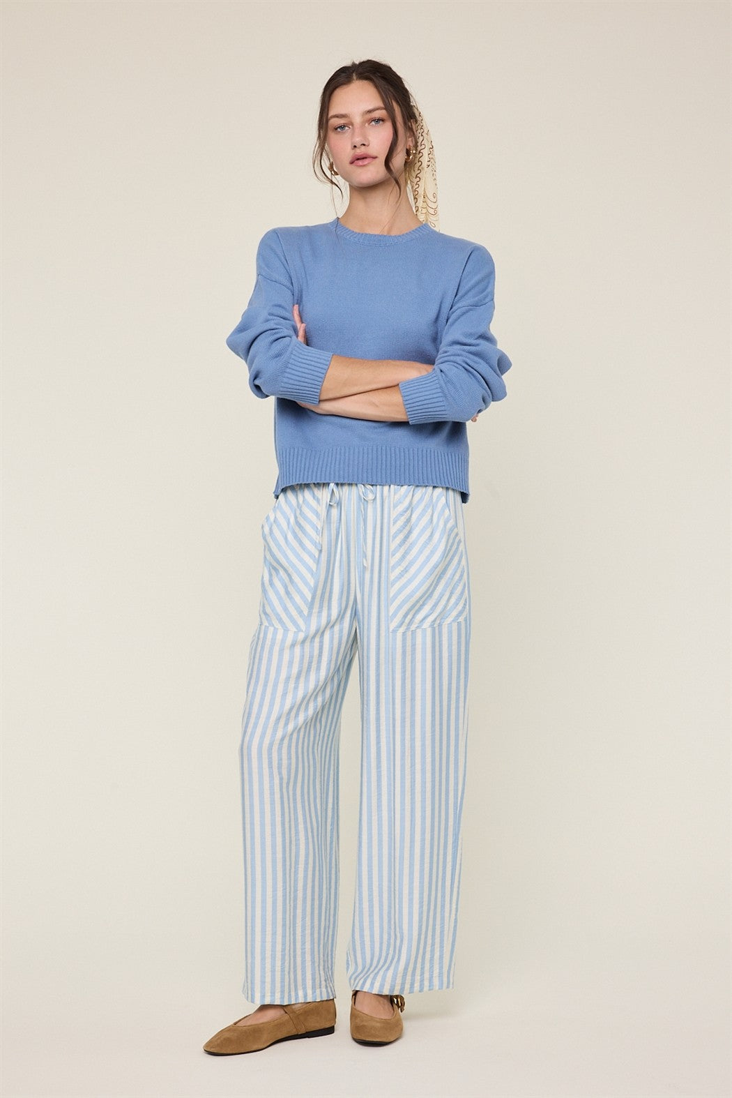 Woman wearing sky blue and cream striped wide-leg pants and blue top on a plain background