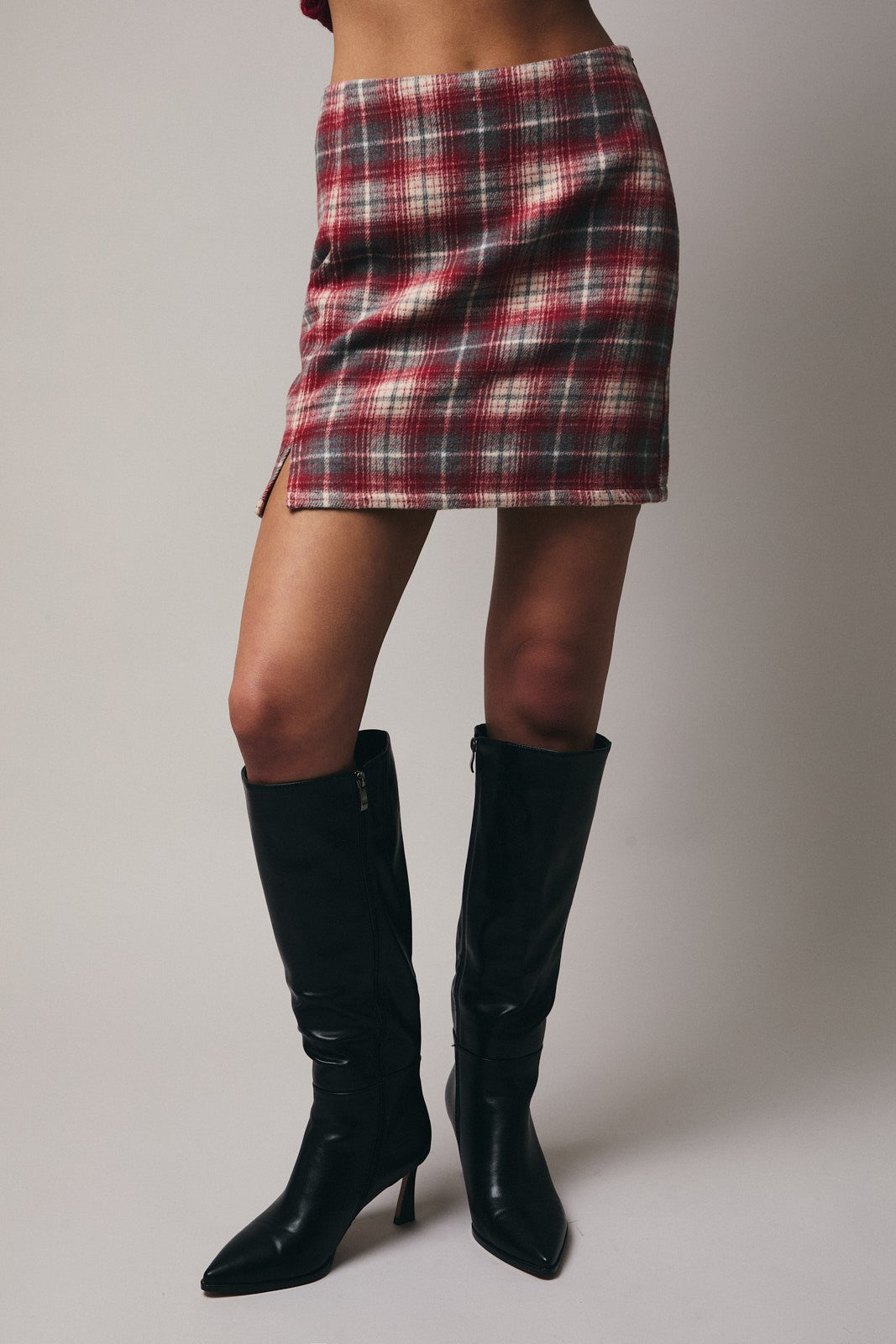 Woman wearing a plaid skirt and black knee-high boots on a plain background