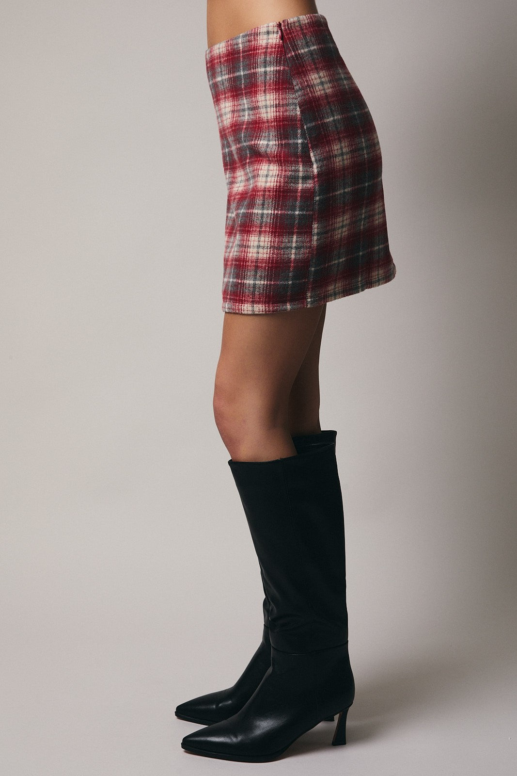 Woman wearing a plaid skirt and black knee-high boots on a plain background