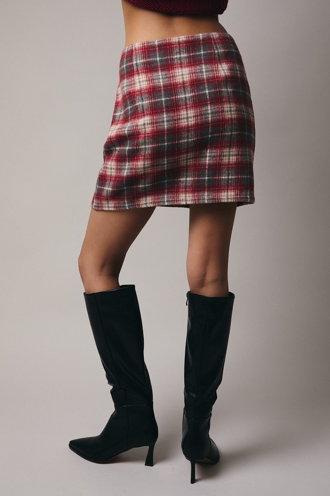 Back view of a woman wearing a plaid skirt and black knee-high boots on a plain background
