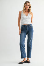 Woman wearing a white tank top with black patterns and blue jeans on a white background