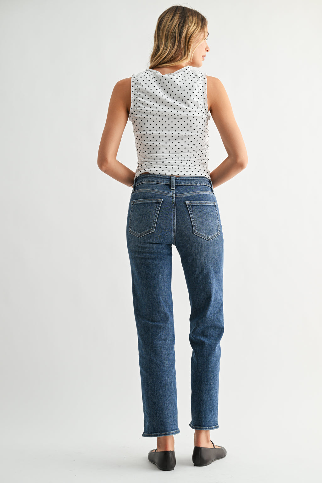 Back view of a woman wearing a patterned top and blue jeans on a white background