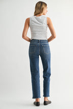 Back view of a woman wearing a patterned top and blue jeans on a white background