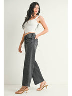 A woman wearing a pair of washed grey straight leg jeans, paired with a white crop top and beige flat sandals, standing against a plain off-white studio background.