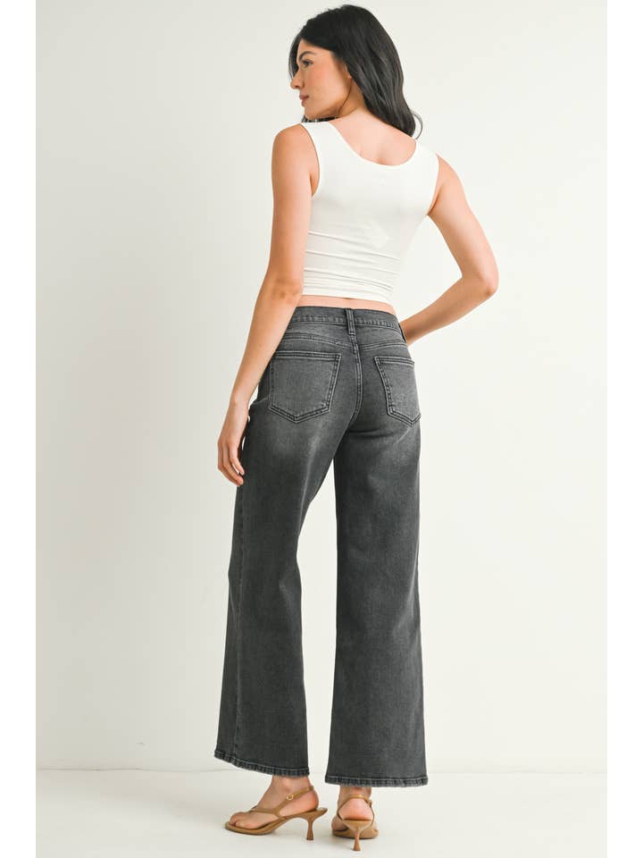 A woman shown from the back wearing a pair of washed grey straight leg jeans, paired with a white crop top and beige flat sandals, standing against a plain off-white studio background.