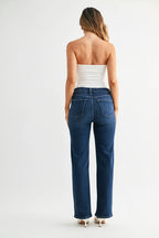 Back view of a woman wearing dark denim mid-rise straight leg jeans and a strapless top on a white background