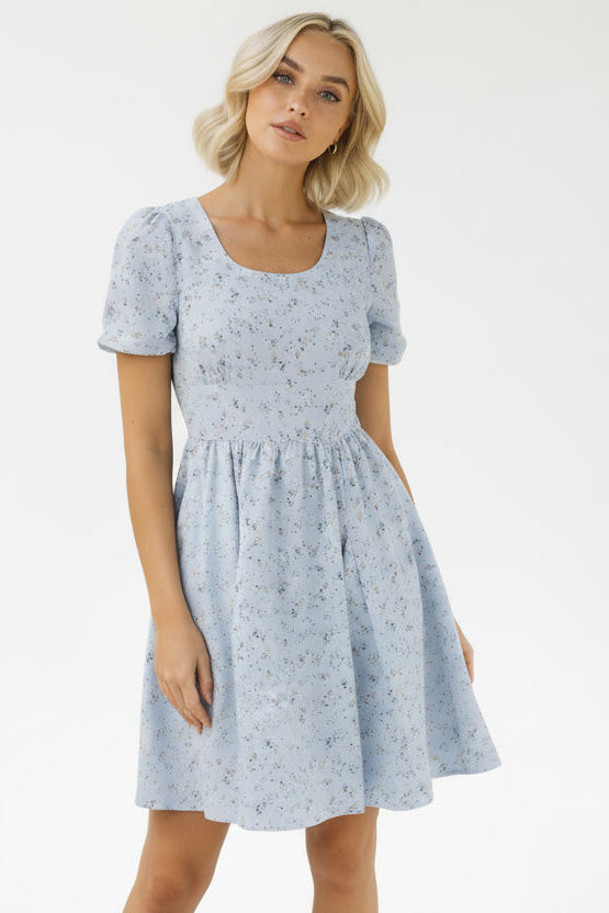 Woman wearing a light blue floral dress against a plain background