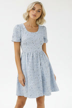 Woman wearing a light blue floral dress against a plain background