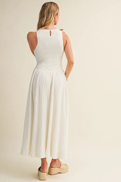 Back view of a woman wearing an off white bubble texture maxi dress on a plain background