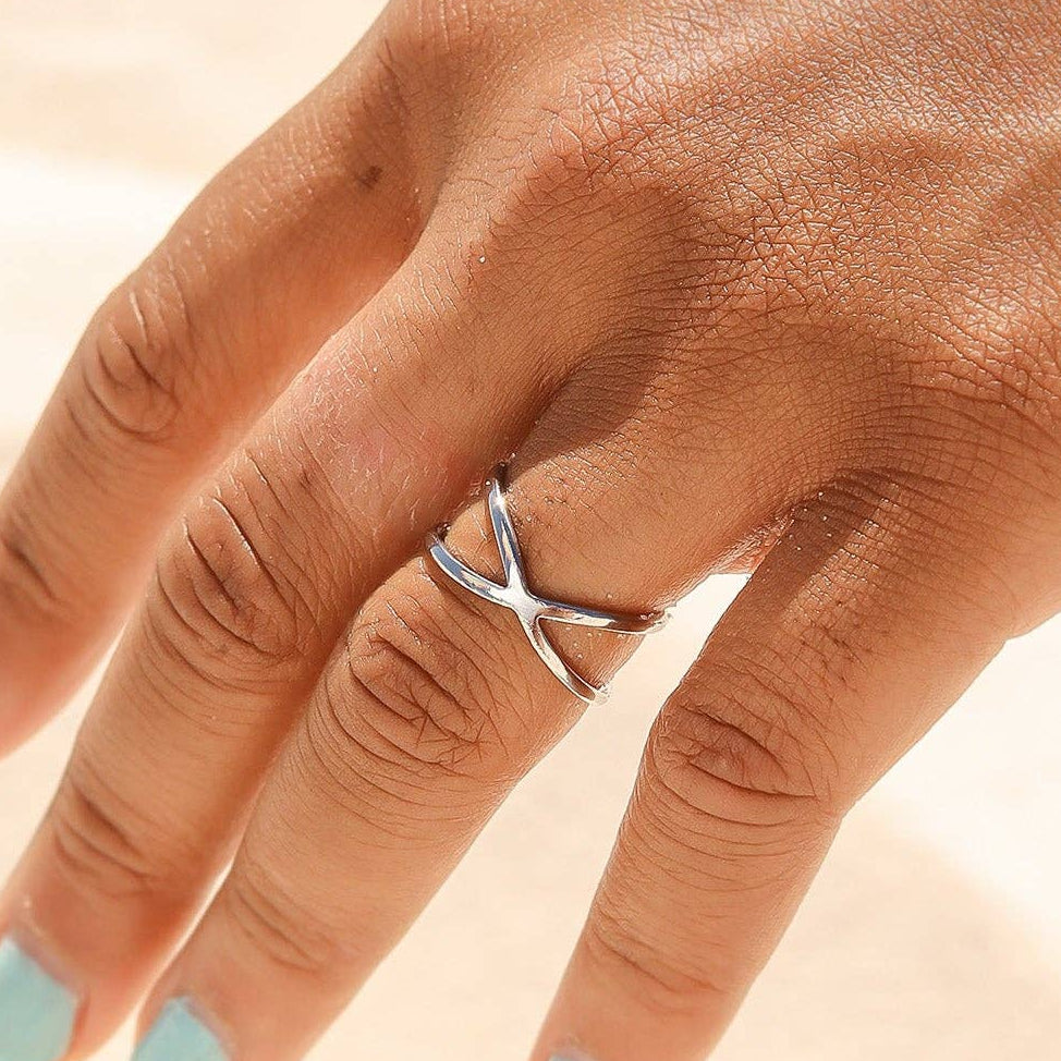 Woman wearing a criss cross silver ring with a light background