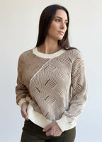 Woman wearing a mocha and cream two-tone sweater design standing against a brick wall.