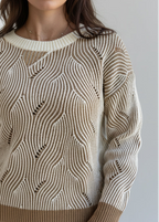 Close-up of a woman wearing a mocha and cream two-tone sweater standing against a brick wall.