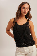 Woman wearing a black open crochet top and white shorts on a plain background
