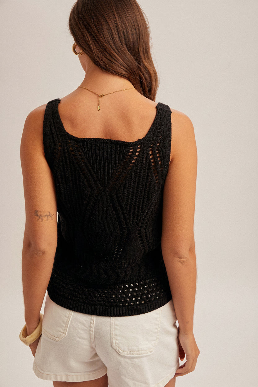 Back view of a woman wearing a black open crochet top and white shorts on a plain background