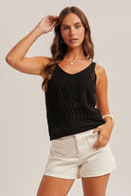 Woman wearing a black open crochet top and white shorts on a plain background