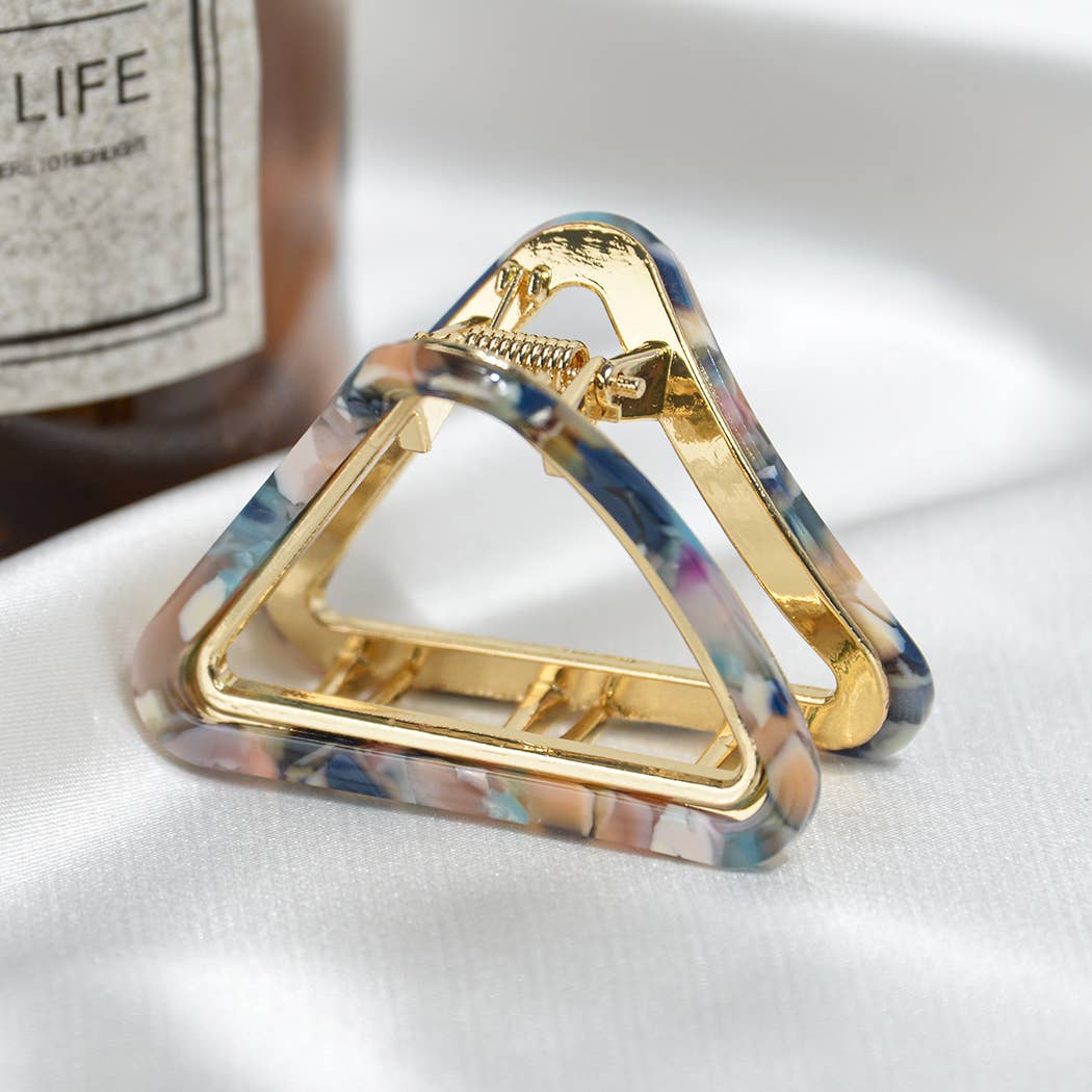 Triangular hair clip with gold finish and multicolor design on a white surface