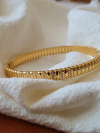 Gold bracelet with textured design on a white fabric background