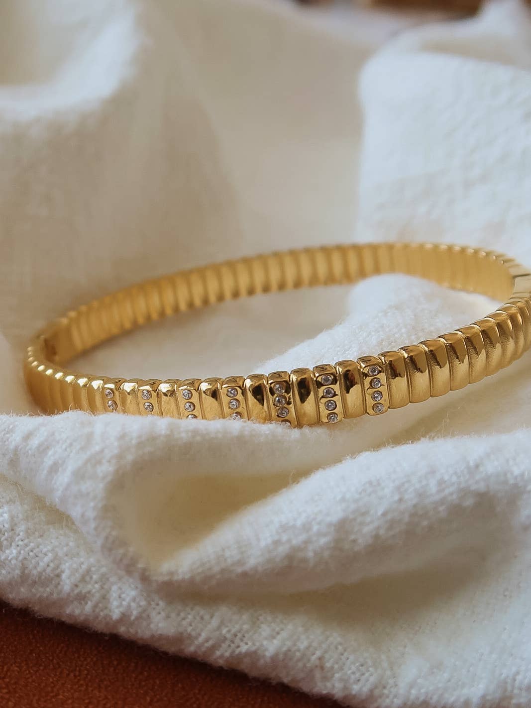 Gold bracelet with textured design on a white fabric background