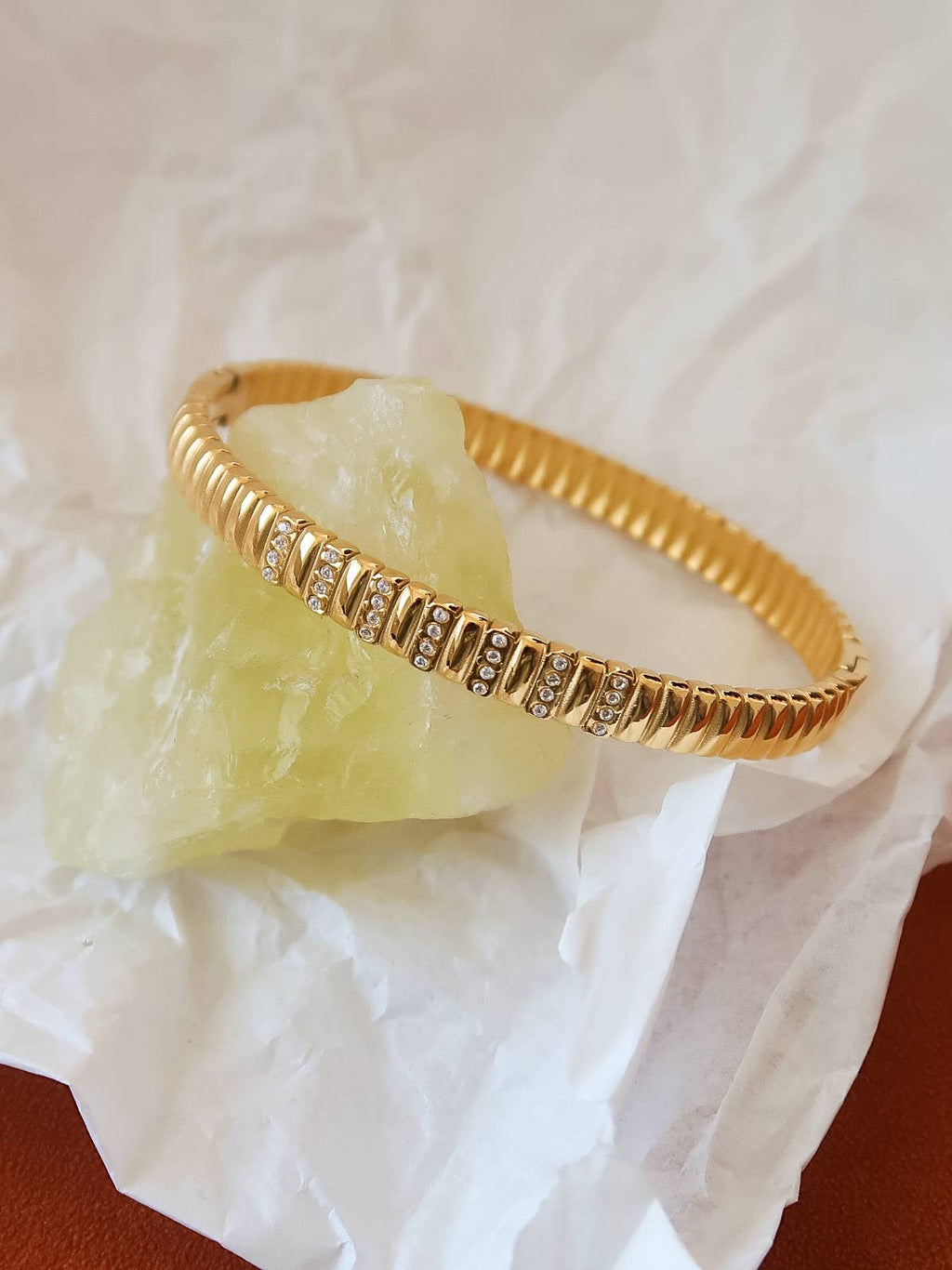 Gold bracelet with small stones on a white fabric background