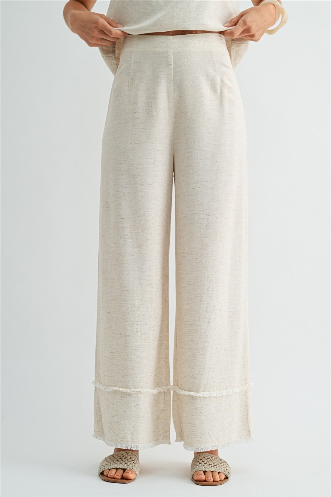 Woman wearing natural wide-leg pants with frayed detail on a plain background