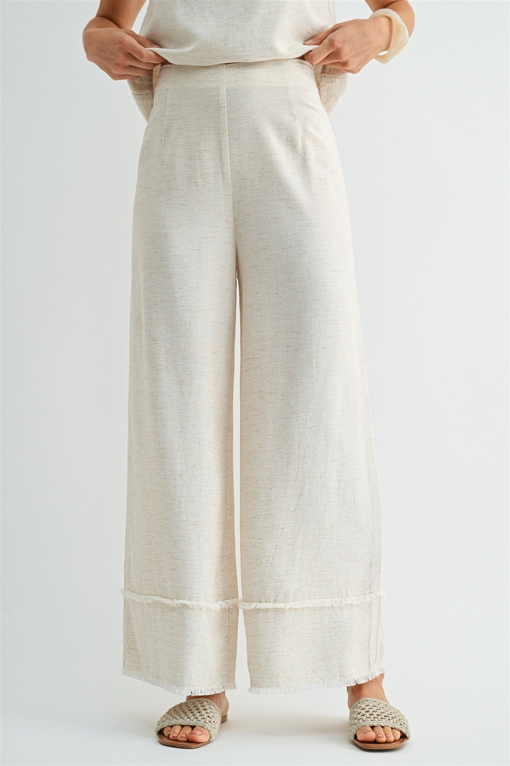 Woman wearing natural wide-leg pants with frayed detail on a plain background