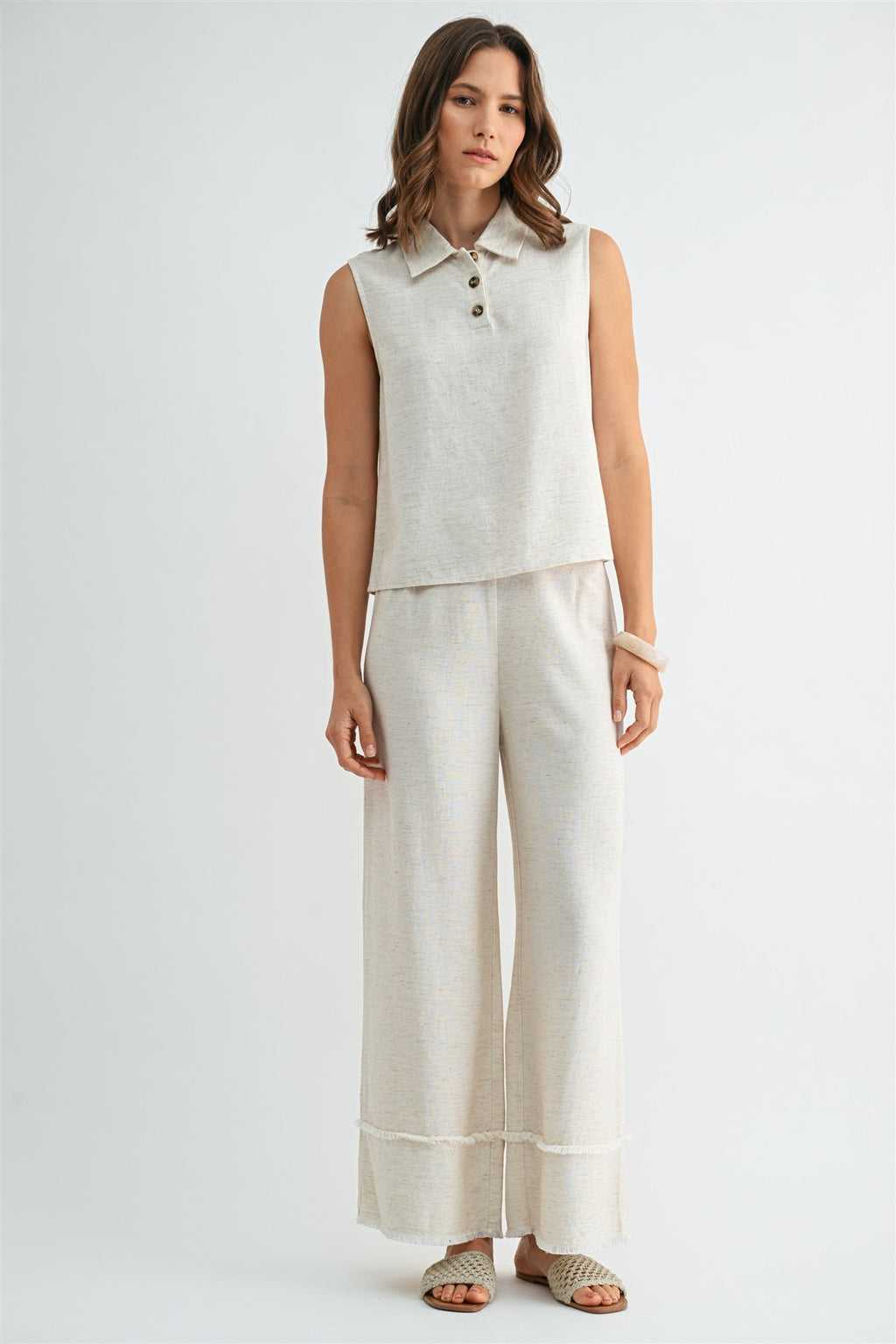 Woman wearing natural wide-leg pants with frayed detail on a plain background