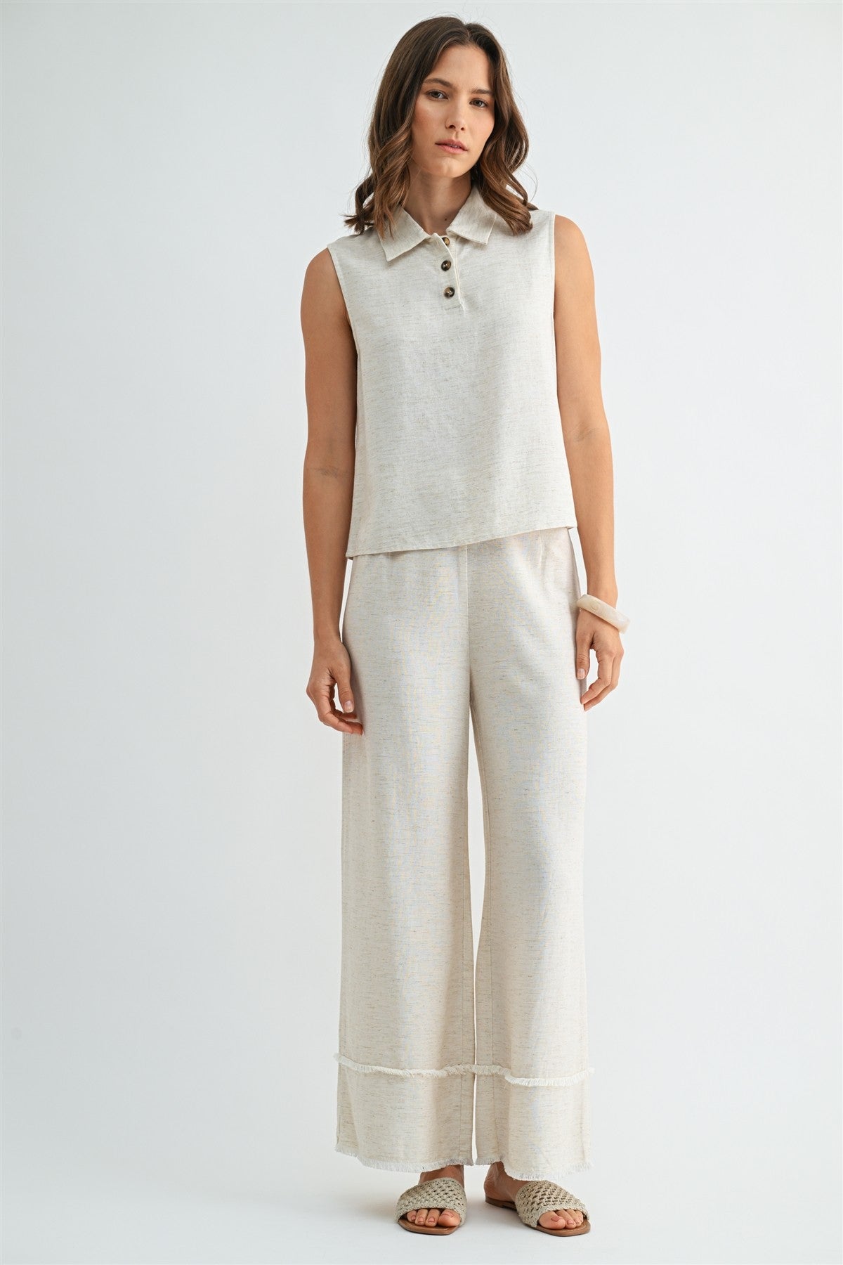 Woman wearing natural wide-leg pants with frayed detail on a plain background