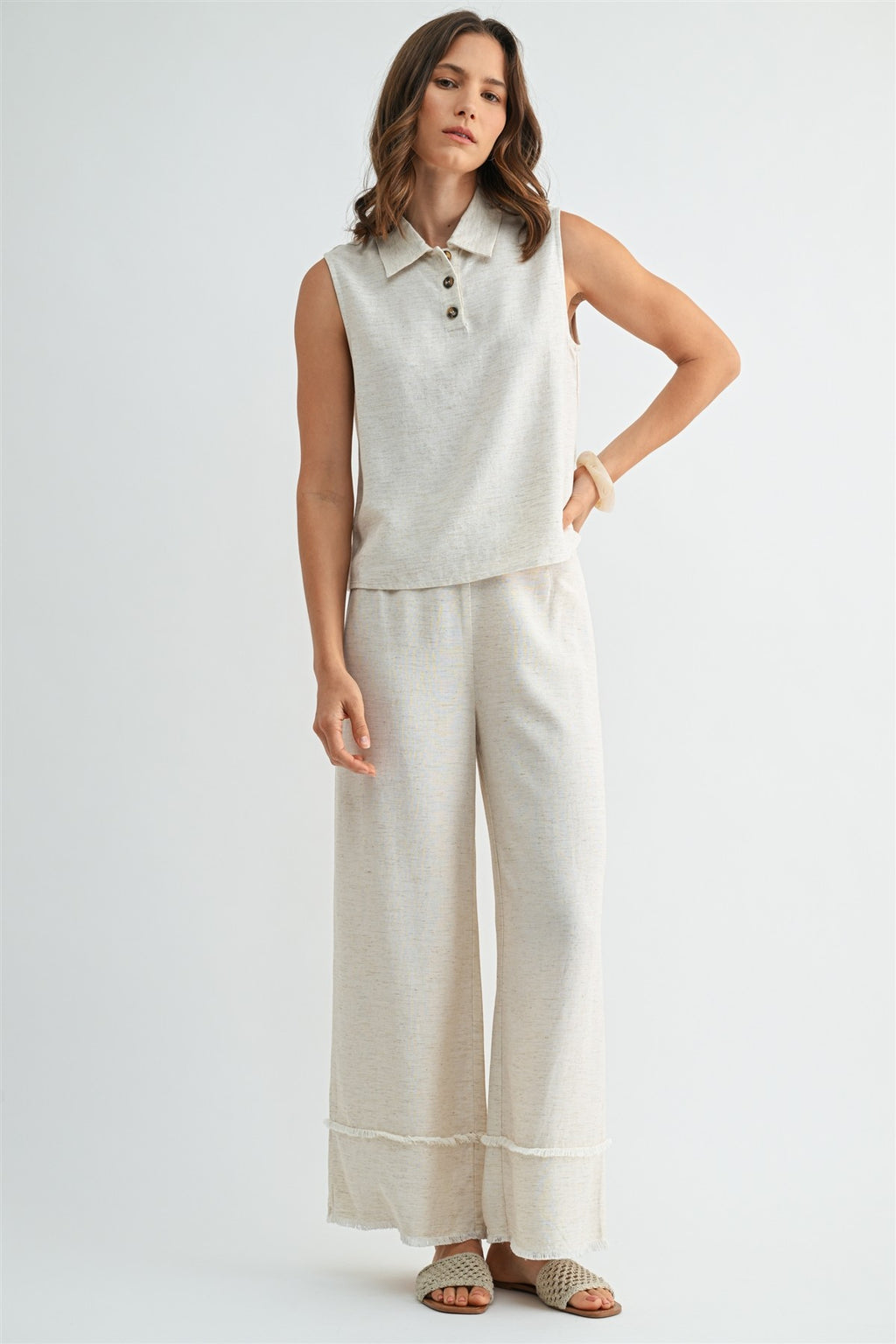 Woman wearing natural wide-leg pants with frayed detail on a plain background