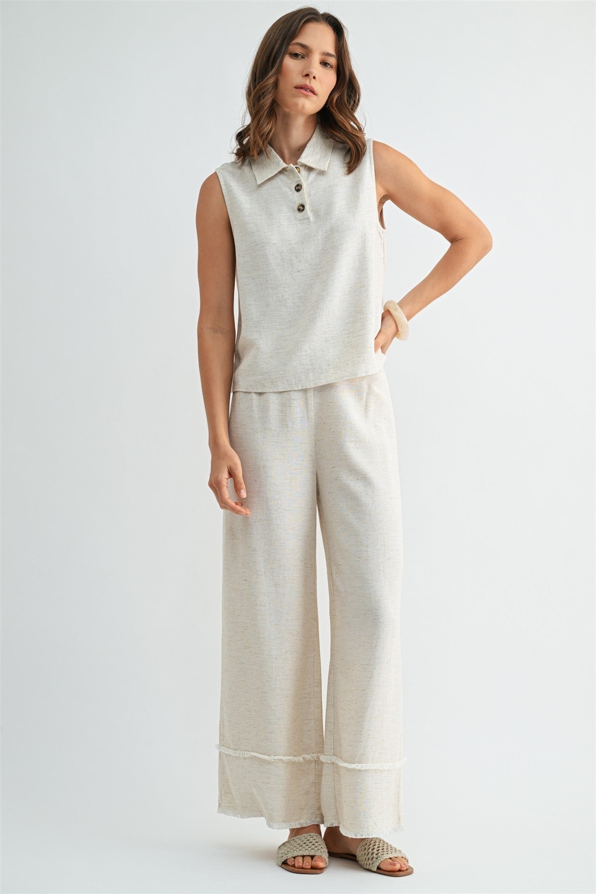 Woman wearing natural wide-leg pants with frayed detail on a plain background