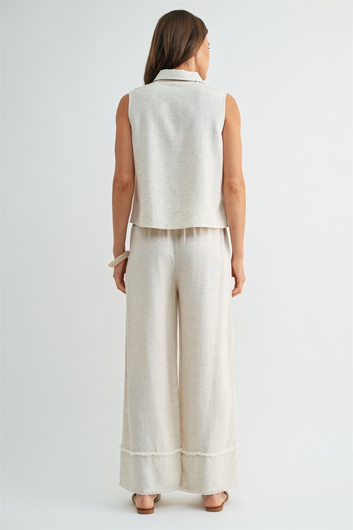 Back view of a woman wearing natural wide-leg pants with frayed detail on a plain background