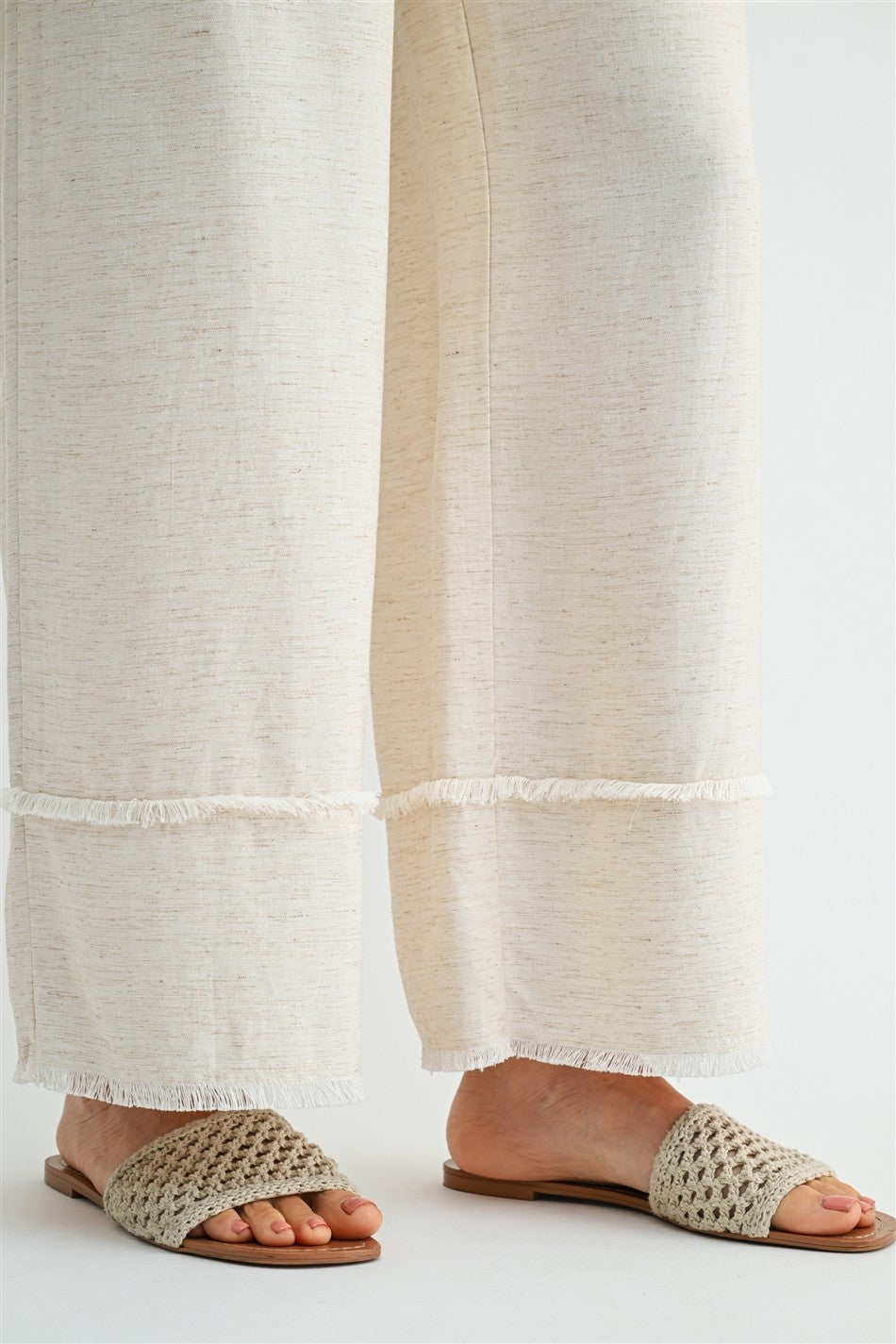 Woman wearing natural wide-leg pants with frayed detail on a plain background
