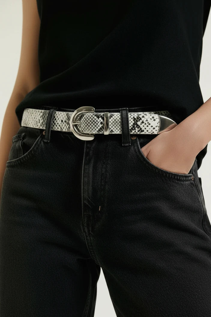 Woman wearing embossed snake pattern belt with silver buckle with jeans and black shirt on white background