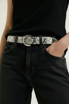 Woman wearing embossed snake pattern belt with silver buckle with jeans and black shirt on white background