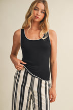Woman wearing a black tank top with white contrast trim and striped pants on a beige background