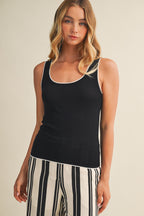Woman wearing a black tank top with white contrast trim and striped pants on a beige background
