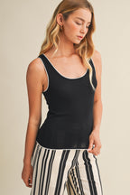 Woman wearing a black tank top with white contrast trim and striped pants on a beige background