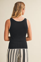 Back view of a woman wearing a black tank top with white contrast trim and striped pants on a beige background