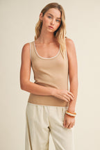 Woman wearing a latte knit tank top and pants against a beige background